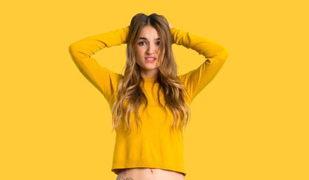 young girl with yellow sweater takes hands on head because has migraine on isolated yellow backgroundの写真素材