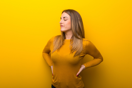Young woman on yellow background suffering from backache for having made an effortの写真素材