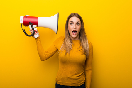 Young woman on yellow background taking a megaphone that makes a lot of noiseの写真素材