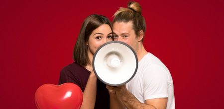 Couple in valentine day shouting through a megaphone over red backgroundの写真素材