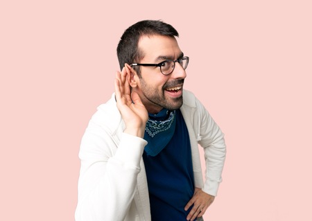 Handsome man with glasses listening to something by putting hand on the ear on isolated pink backgroundの写真素材