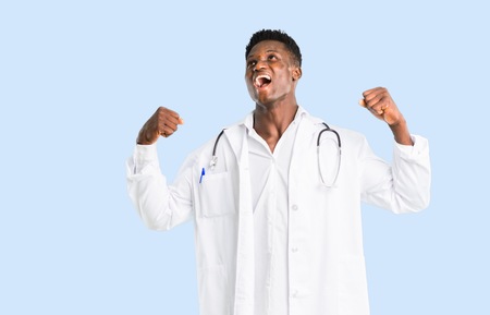 African american doctor celebrating a victory in winner position on isolated blue backgroundの写真素材