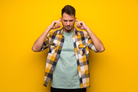 Handsome man over yellow wall frustrated and covering ears with handsの写真素材