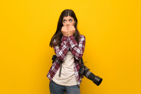 Photographer teenager girl over yellow wall nervous and scared putting hands to mouthの写真素材