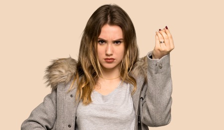 Teenager girl with coat making Italian gesture on isolated yellow backgroundの写真素材