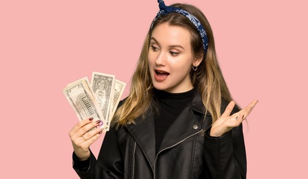 Teenager girl with leather jacket taking a lot of money on isolated pink backgroundの写真素材