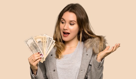 Teenager girl with coat taking a lot of money on isolated yellow backgroundの写真素材