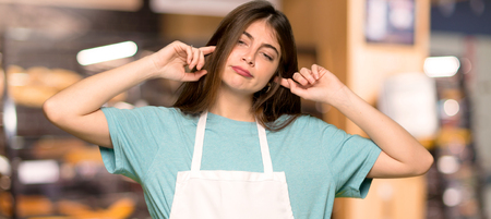 Girl with apron covering both ears with hands in a bakeryの写真素材