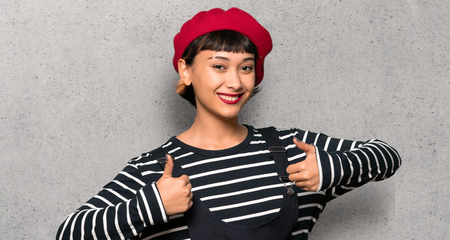Young woman with beret with thumbs up because something good has happened over textured wallの写真素材