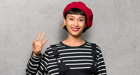 Young woman with beret happy and counting three with fingers over textured wallの写真素材