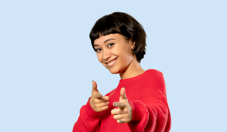 Short hair girl with red sweater pointing to the front and smiling on isolated blue backgroundの写真素材