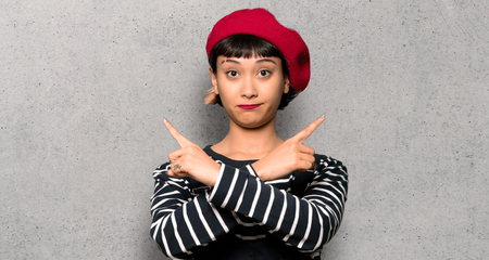 Young woman with beret pointing to the laterals having doubts over textured wallの写真素材