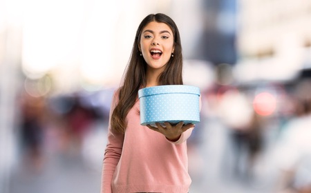 Teenager girl with pink shirt holding a gift in hands at city