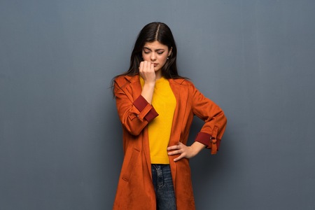 Teenager girl with coat over grey wall having doubtsの写真素材