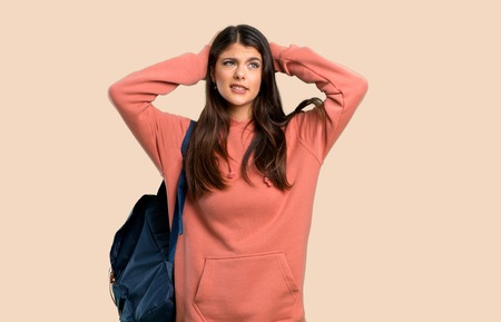 Teenager girl with sweatshirt and backpack takes hands on head because has migraine on color backgroundの写真素材