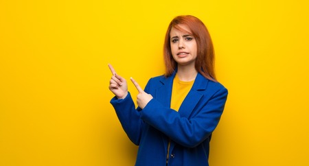 Young redhead woman with trench coat frightened and pointing to the sideの写真素材