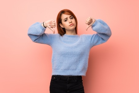 Young redhead woman over pink background showing thumb down with both handsの写真素材