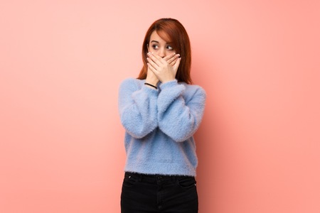 Young redhead woman over pink background covering mouth with handsの写真素材