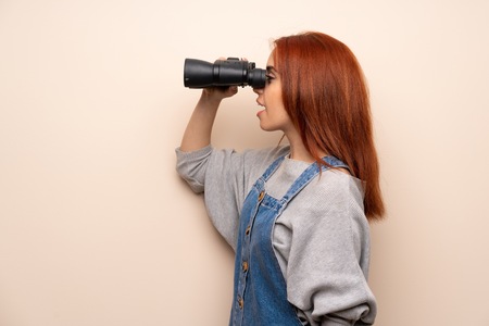 Young redhead woman over isolated background and looking in the distance with binocularsの写真素材
