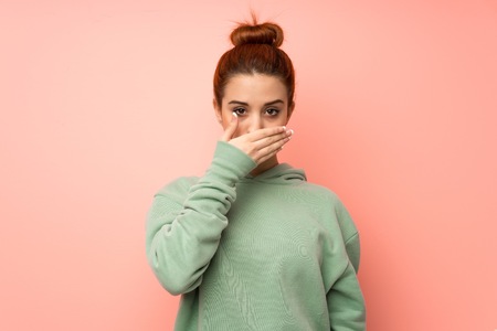 Young redhead woman with sweatshirt covering mouth with hands for saying something inappropriateの写真素材