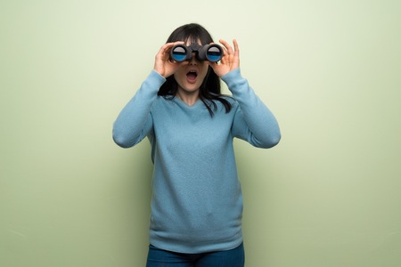 Young woman over green wall and looking in the distance with binocularsの写真素材