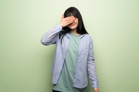 Young woman over green wall covering eyes by hands. Do not want to see somethingの写真素材