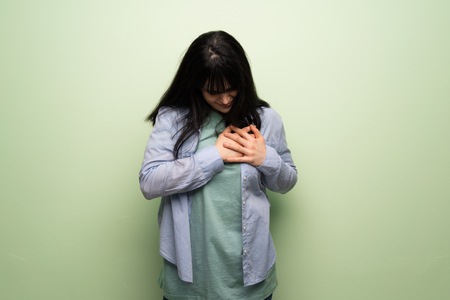 Young woman over green wall having a pain in the heartの写真素材