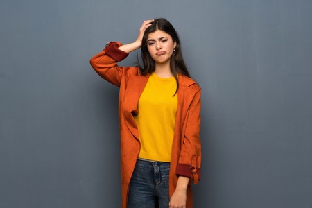 Teenager girl with coat over grey wall with an expression of frustration and not understandingの写真素材