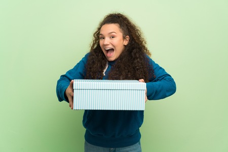 Teenager girl over green wall surprised because has been given a gift