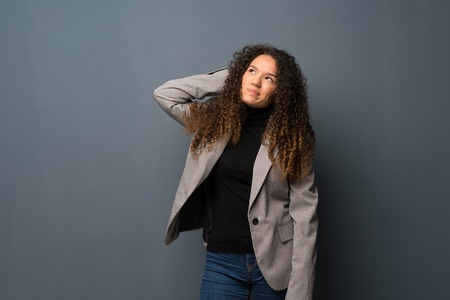Teenager girl over blue wall having doubts while scratching headの写真素材