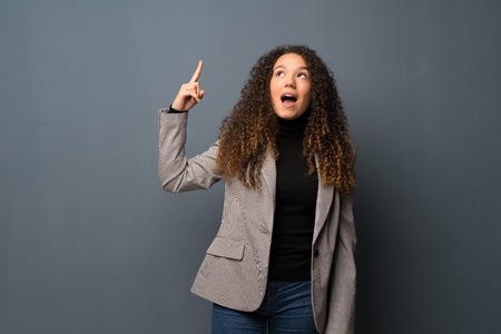 Teenager girl over blue wall intending to realizes the solution while lifting a finger upの写真素材