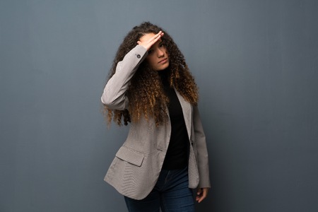 Teenager girl over blue wall looking far away with hand to look somethingの写真素材