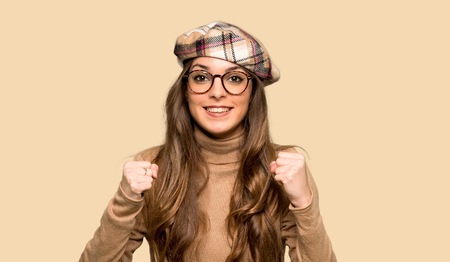 Young woman with beret celebrating a victory in winner position over isolated yellow backgroundの写真素材
