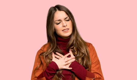 Young woman with coat having a pain in the heart over isolated pink background