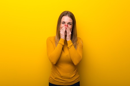 Young woman on yellow background smiling a lot while covering mouthの写真素材