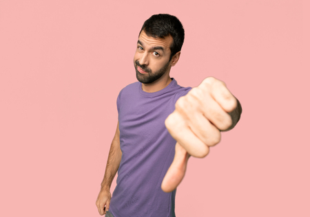 Handsome man showing thumb down sign with negative expression on isolated pink background