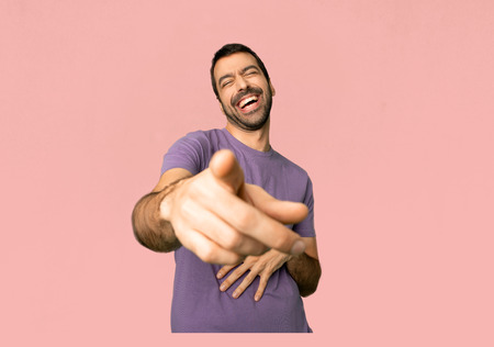 Handsome man pointing with finger at someone and laughing a lot on isolated pink backgroundの写真素材