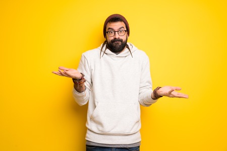 Hippie man with dreadlocks making unimportant gesture while lifting the shoulders