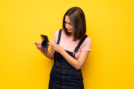 Young woman over yellow wall holding a walletの写真素材