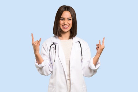 Young doctor woman making rock gesture on isolated blue backgroundの写真素材
