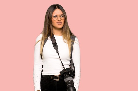 Young photographer woman is a little bit nervous and scared pressing the teeth on isolated pink backgroundの写真素材