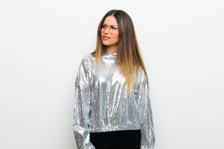 Young woman with glasses over white wall is a little bit nervous and scared pressing the teethの写真素材