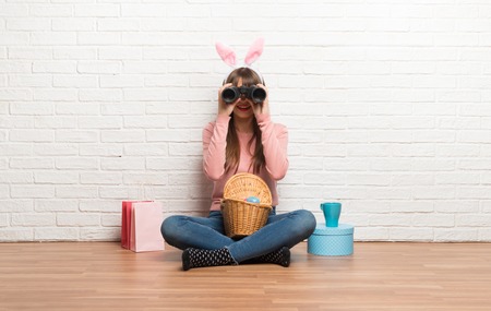 Woman with bunny ears for Easter holidays sitting on the floor and looking for something in the distance with binocularsの写真素材