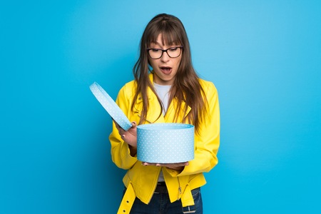 Young woman with yellow jacket on blue background holding a gift in hands