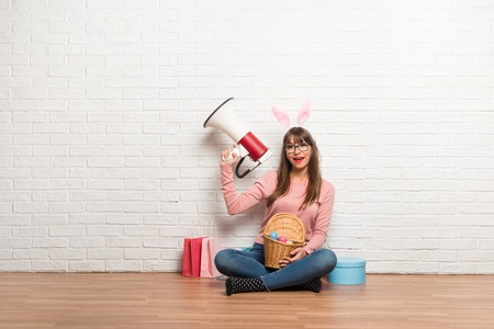 Woman with bunny ears for Easter holidays sitting on the floor holding a megaphone