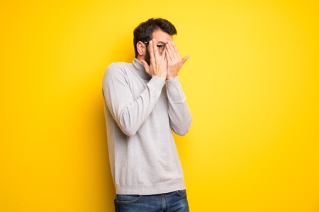 Man with beard and turtleneck covering eyes by hands and looking through the fingersの写真素材