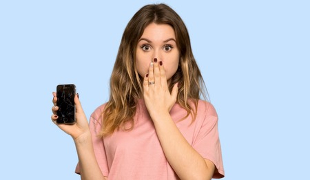 Teenager girl with pink sweater with a broken phone on isolated blue backgroundの写真素材