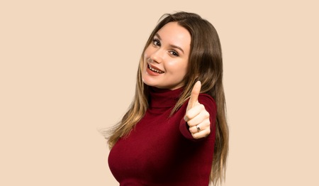 Teenager girl with turtleneck with thumbs up because something good has happened over isolated ocher...