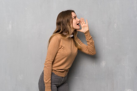 Teenager girl over textured wall shouting with mouth wide open to the lateralの写真素材