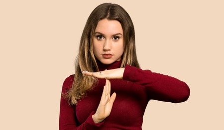 Teenager girl with turtleneck making time out gesture over isolated ocher background